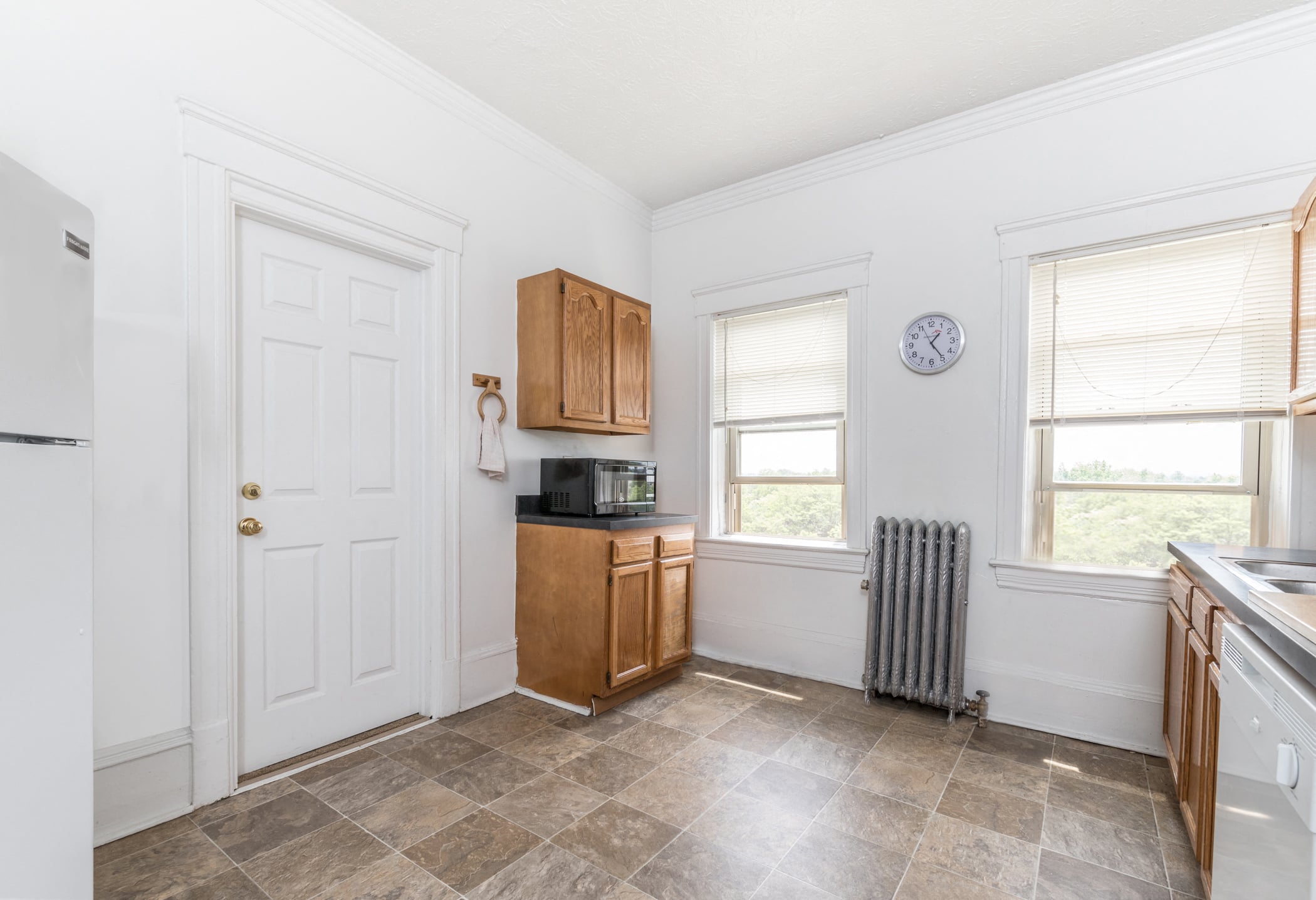 A kitchen with a white door, brown cabinets, and a tiled floor.